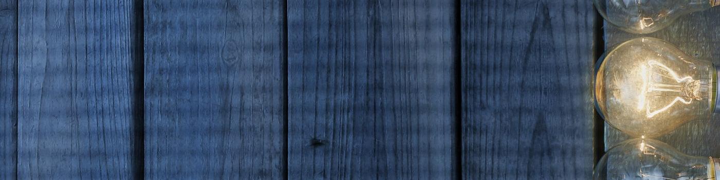 5 lightbulbs against wooden background with one lit up