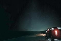 Man standing against car under a starlit sky looking at his phone