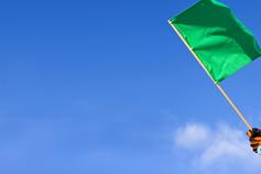 A hand holding a geen "go" race flag