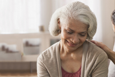Old woman with grey short hair looking down smiling and sitting on sofa
