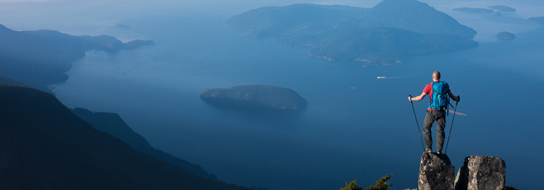 Back view of a mountain climber wearing red shirt and blue bag against blue sky