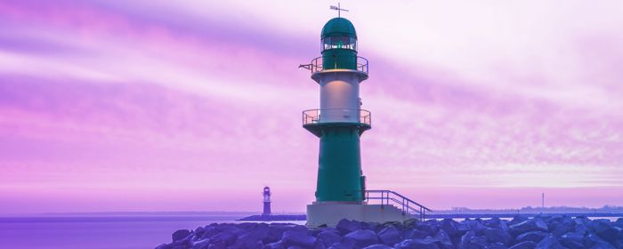 Faro de luz a la orilla del mar. El fondo es un degradado de purpura a azul cobalto