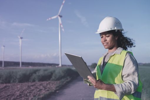 Engineer woman working with laptop outdoor near wind turbine at background