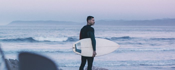 Surfista de mediana edad mira hacia la playa en la hora azul