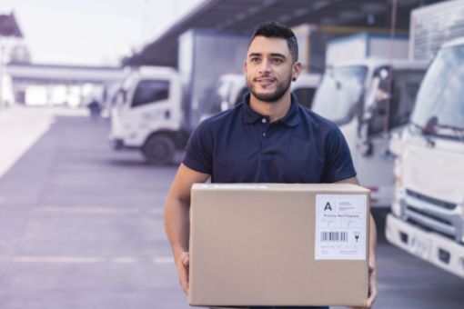 Hombre trabajando en un almacén de distribución y llevando una caja hacia un camión
