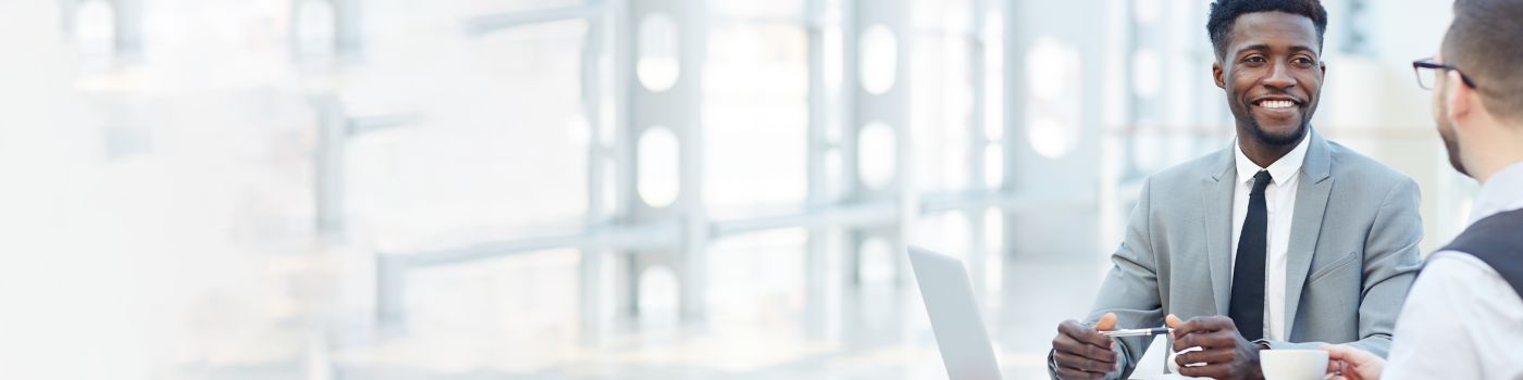 doi homems conversando sentados em uma mesa com o laptop aberto