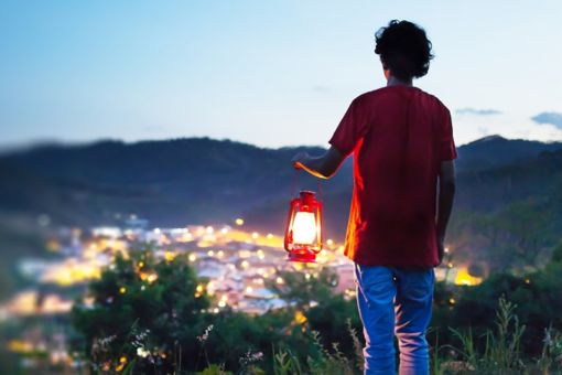 Man holding lantern on a hill over-looking over lit up city