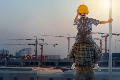 Boy sitting on man’s shoulders looking at construction site