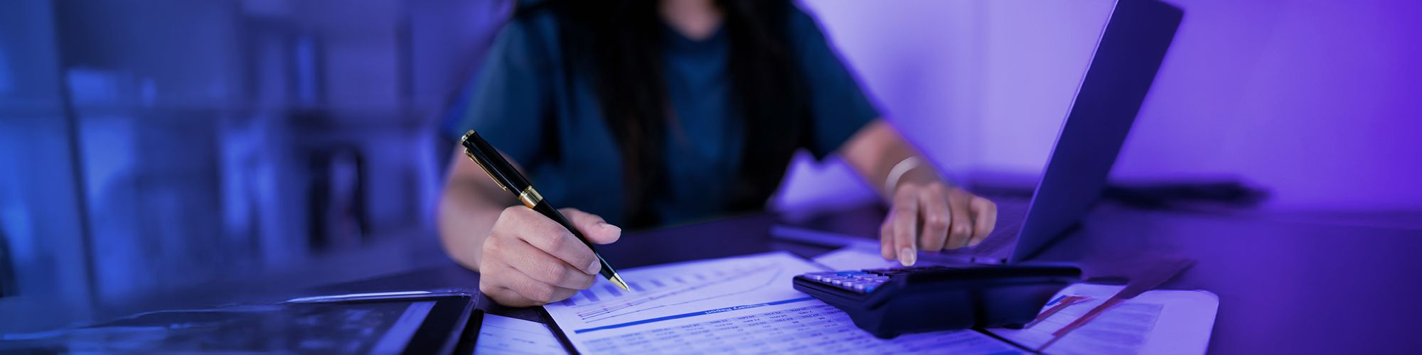 A woman is typing something on a calculator and writing something down on paper.