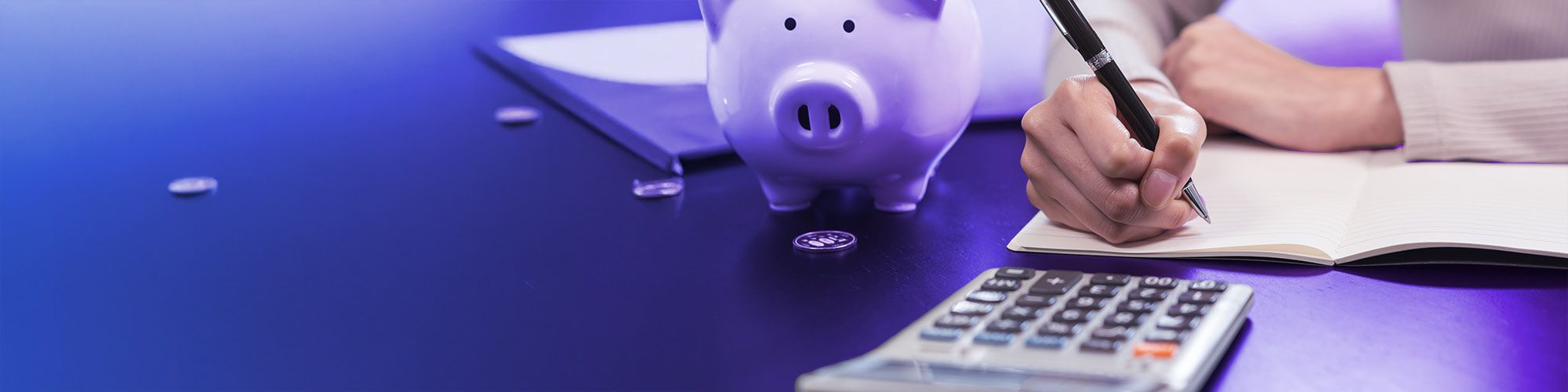 Someone is writing something down on paper and there is a calculator and a piggybank on the table