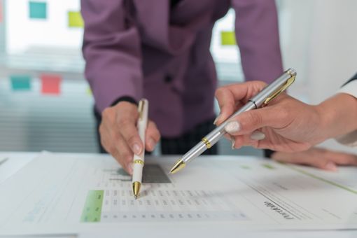 Two people using pens to mark a document on a table
