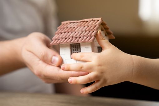 De handen van een vrouw en kind houden een miniatuurhuisje vast