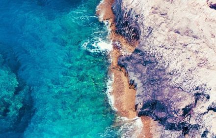 Birds-eye-view of clear blue sea meeting cliffs