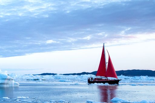 Red sailboat sailing through icebergs