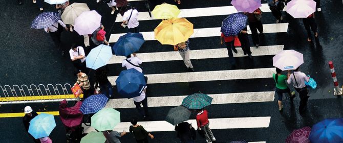 Insurance | Crowd crossing a street carrying open umbrellas 