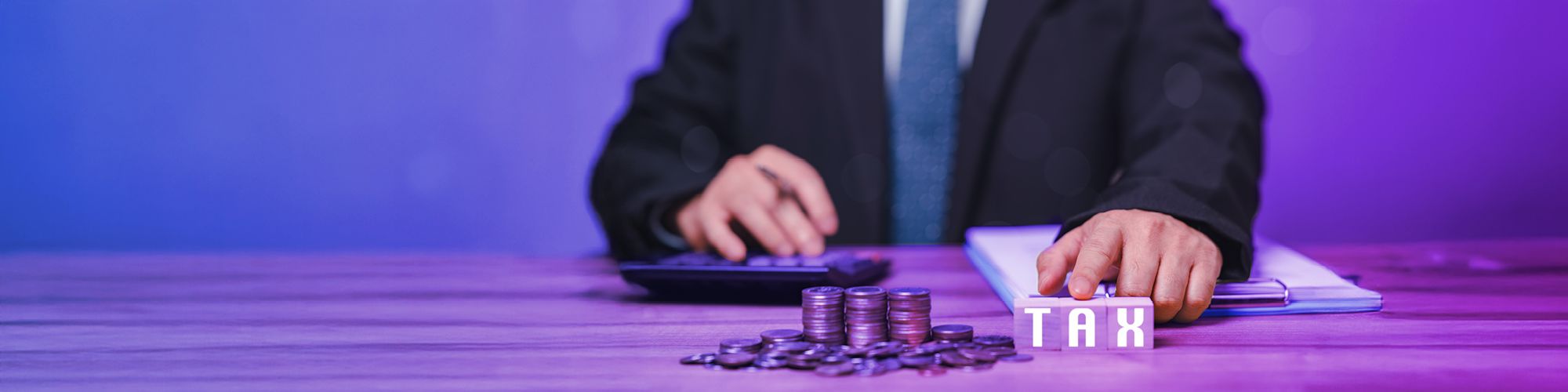 A hand on a desk with coins, and die with the letters of the word TAX