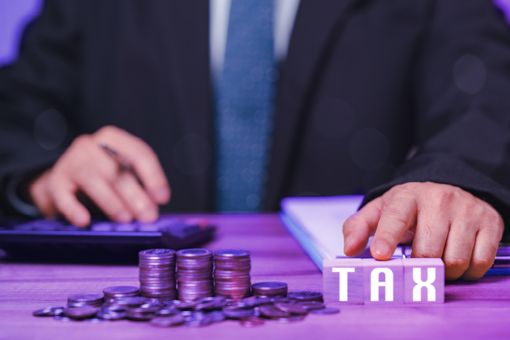 A hand on a desk with coins, and die with the letters of the word TAX