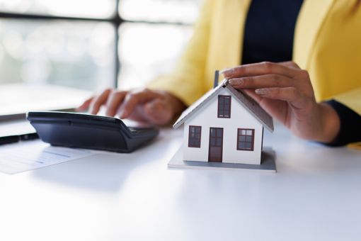 A woman is typing something on a calculator and holding her hand above a miniature house