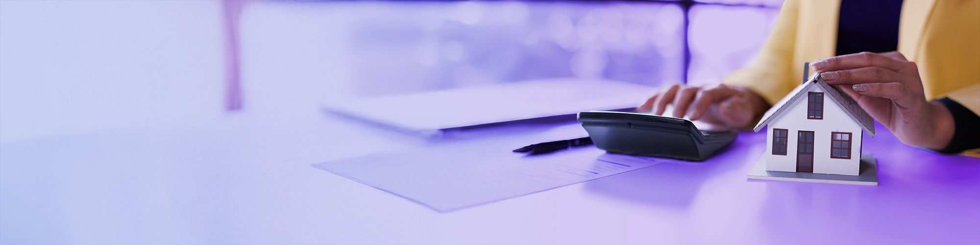 A woman is typing something on a calculator and holding her hand above a miniature house