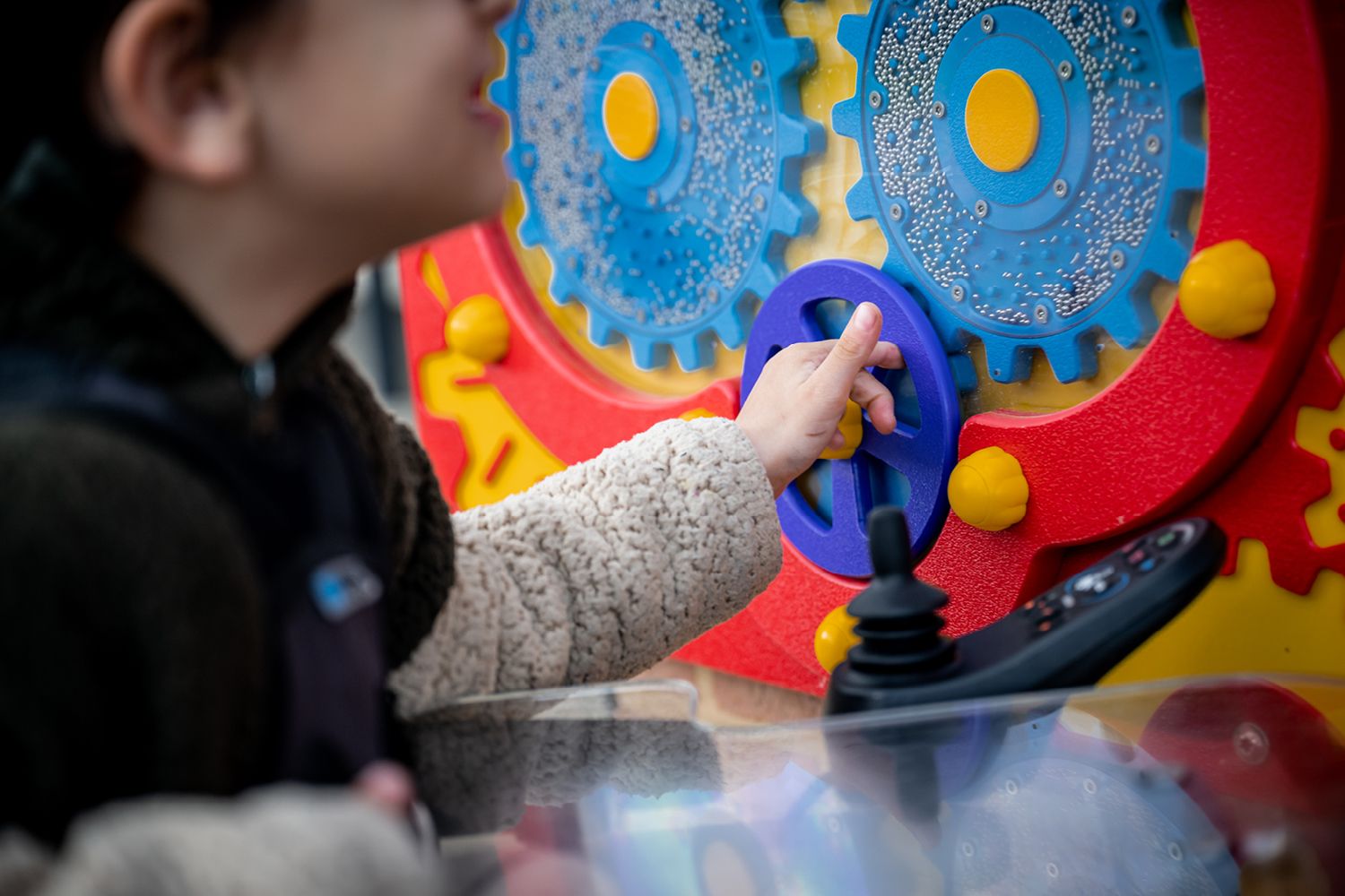 child in wheelchair playing with colorful gears at playground