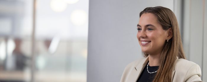 Ung dökkhærð kona situr og brosir framhjá myndavélinni