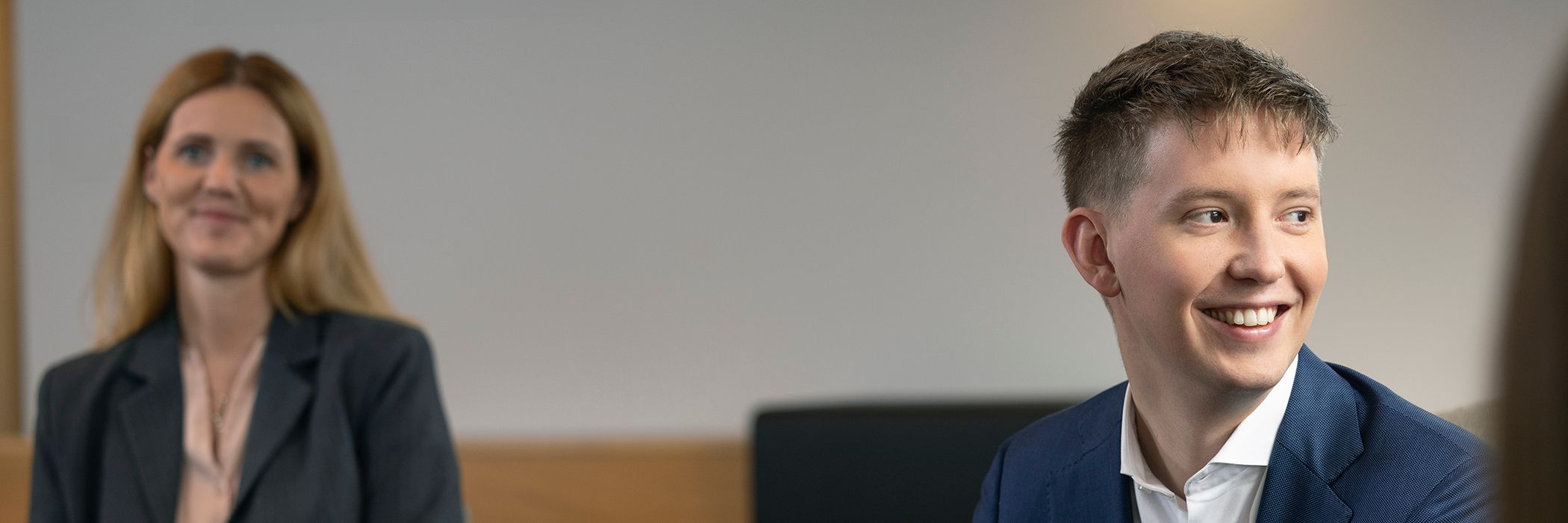 Ung dökkhærð kona situr og brosir framhjá myndavélinni