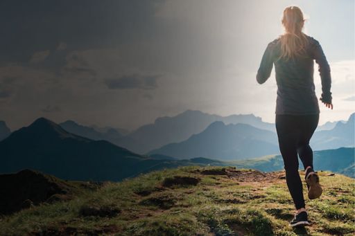 uma moça vista de costas correndo em uma paisagem de montanhas