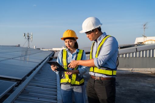 A man and a woman are holding papers and talking with a windmill in the background