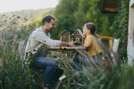 A man and a girl outdoors with insect hotels, fostering biodiversity by supporting pollinators