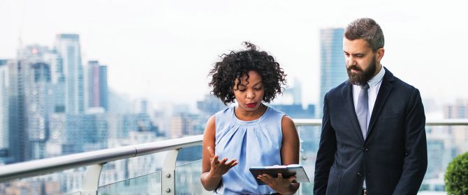 Two businesspeople looking at a tablet, discussing a strategy