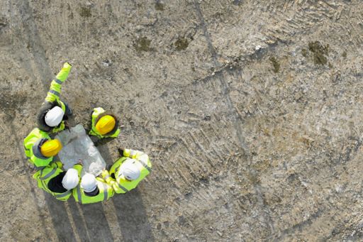 Aerial view of six construction workers wearing yellow & white caps, holding map