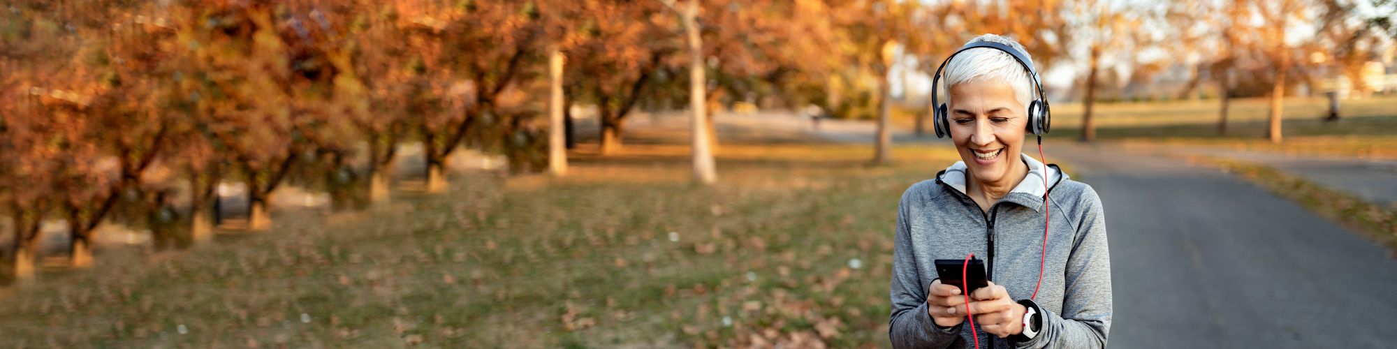 Active senior woman listening to music with headphones on smart phone