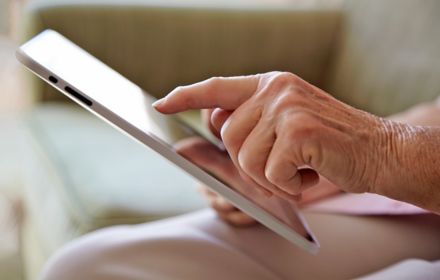 Elderly woman's hand, using tablet computer to look at photos in a retirement home