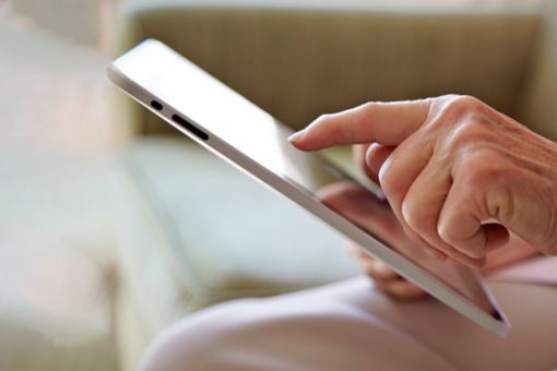 Elderly woman's hand, using tablet computer to look at photos in a retirement home