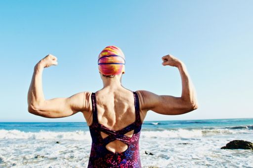 Older Caucasian woman flexing her muscles on beach