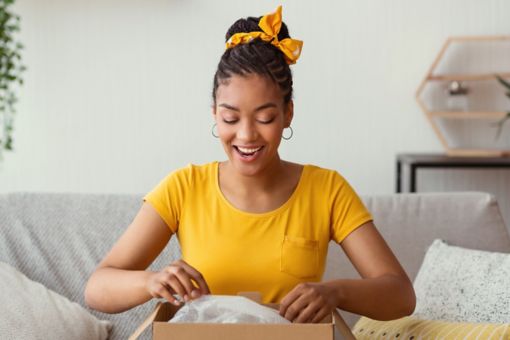 Woman sat on a sofa opening a cardboard box