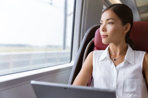 Businesswoman pensive looking out the window while working on computer on travel commute to work.