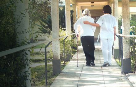 Back view of female doctor helping elderly woman with walker in the hospital garden