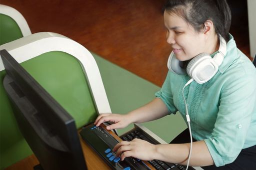 Blind person with headphones using computer with braille