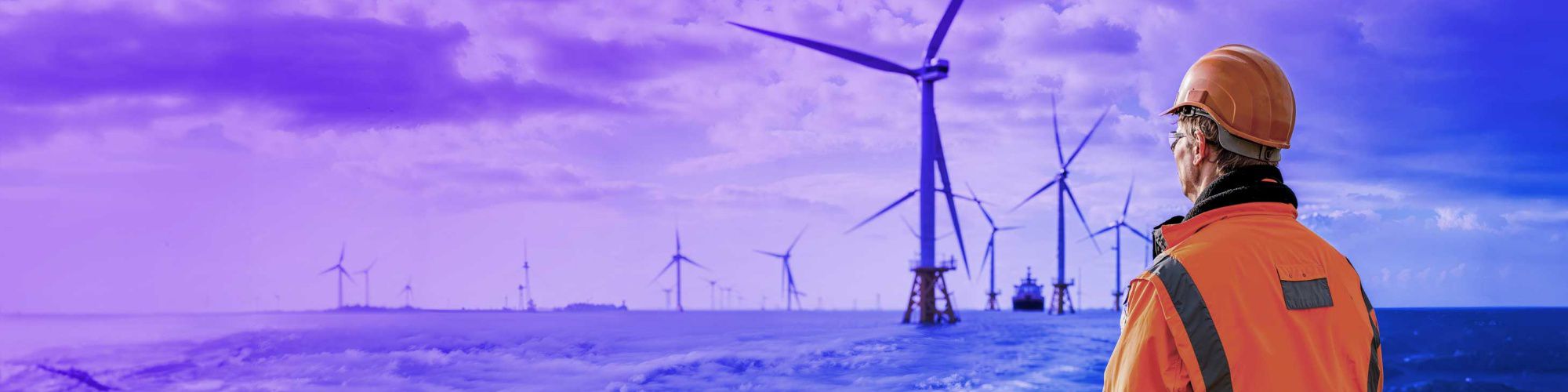 man looking out at the ocean with wind turbines in the background