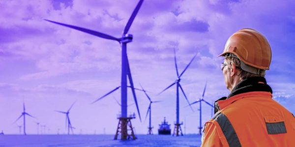 man looking out at the ocean with wind turbines in the background