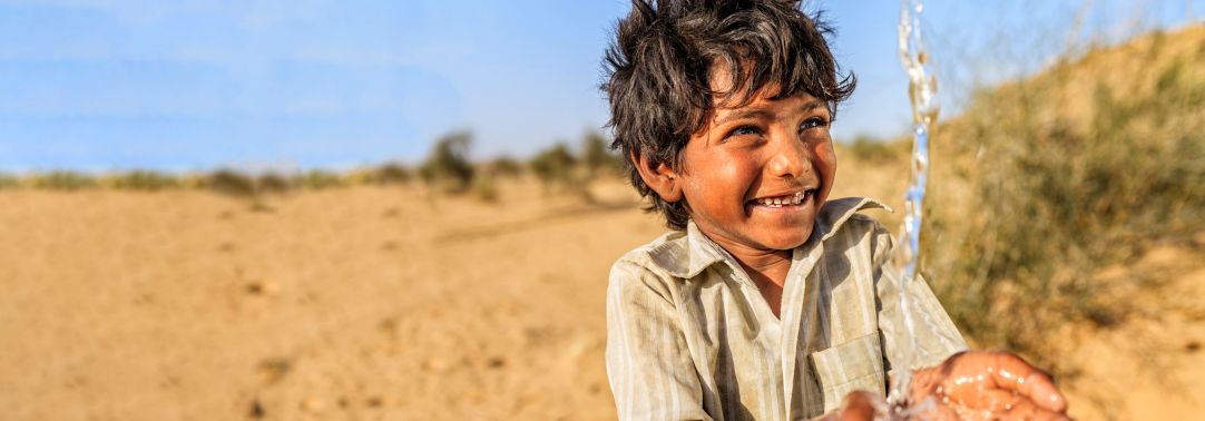 Boy child smiling at touching water sand in the background