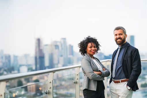 Business woman and man standing by glass railing with city in background