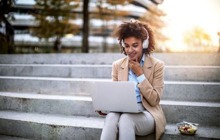 Business woman on a lunch break outdoors using laptop with headphones