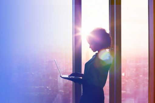 Woman working on laptop at a window in the morning sun