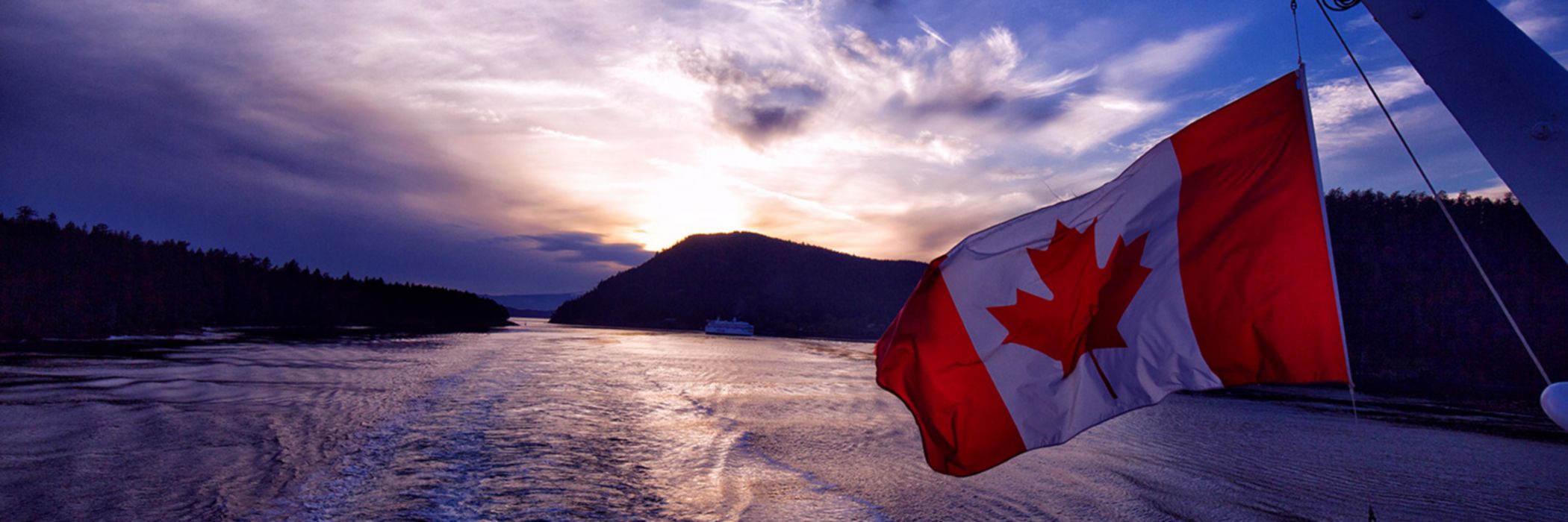 Canadian flag hanging off the back of a boat over water