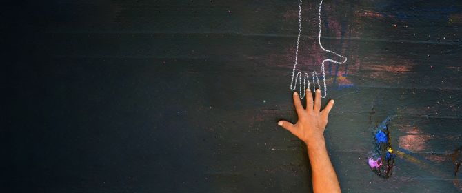 Chalk hand outline with real hand reaching towards it