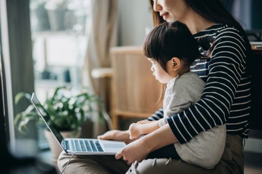 Mother using laptop and working from home while taking care of little daughter
