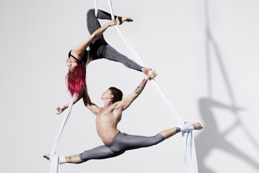 Circus artists in silks with shadows projected on white wall