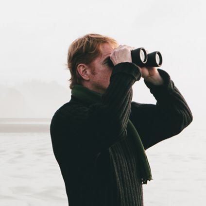 Man looking through binoculars with island in background